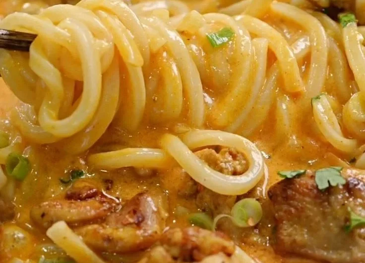 Bowl of Thai coconut red curry chicken udon garnished with fresh herbs