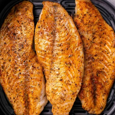 Crispy air fryer tilapia served on a plate with lemon and herbs.