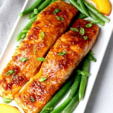 Peach glazed salmon fillet garnished with fresh herbs on a plate.