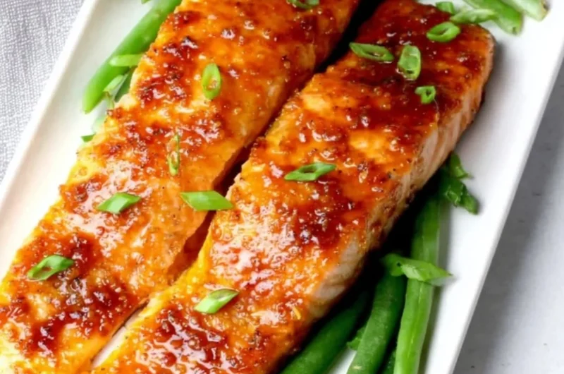 Peach glazed salmon fillet garnished with fresh herbs on a plate.