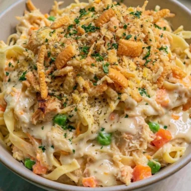 Homemade chicken noodle casserole served in a dish with fresh herbs on top.