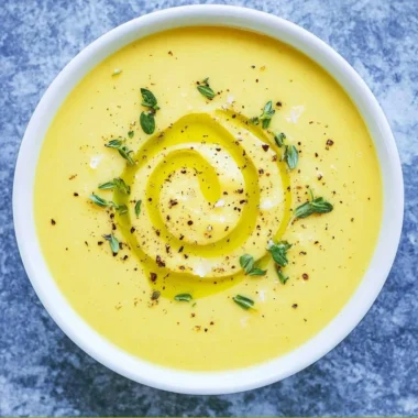 Creamy summer squash soup served in a bowl with fresh herbs on top
