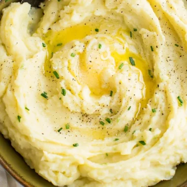 Bowl of perfect creamy mashed potatoes garnished with herbs